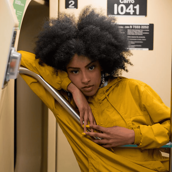 Individual with 4C hair in yellow jacket leaning against metal pole