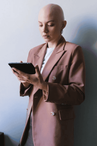 Bald individual in light pink jacket holding tablet