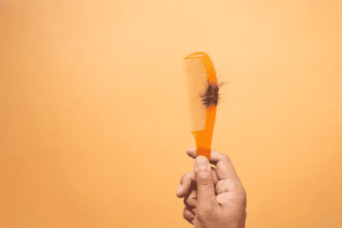 Hand holding orange comb with hair strands